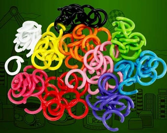 May include: A collection of colorful plastic chain links in various colors, including white, black, yellow, orange, pink, red, green, blue, and purple. The links are arranged in a pile against a green background.