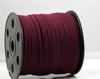 Puede incluir: Un carrete de cordón de ante burdeos. El cordón está enrollado alrededor de un carrete de plástico negro. El cordón de ante es de un tono burdeos profundo y rico, y la textura parece suave y lisa. El carrete está sobre un fondo blanco.