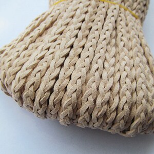 May include: A close-up of a beige braided leather cord. The cord is made of multiple strands of leather that are woven together to create a thick, durable cord.