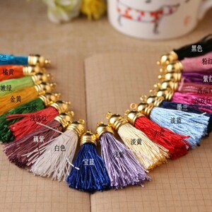 May include: Assortment of 16 colorful tassel trims with gold metal caps. The tassels are arranged in a semi-circle and labeled with their corresponding colors in Chinese characters.