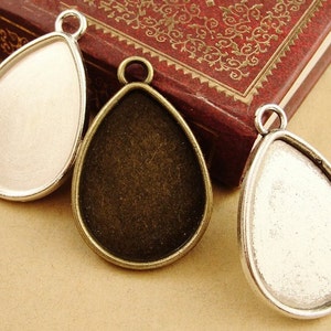 Könnte beinhalten: Drei tropfenförmige Anhänger-Tabletts mit silbernen und bronzenen Oberflächen. Die Tabletts sind so konzipiert, dass sie ein kleines Stück Glas oder anderes Material für die Schmuckherstellung aufnehmen können.