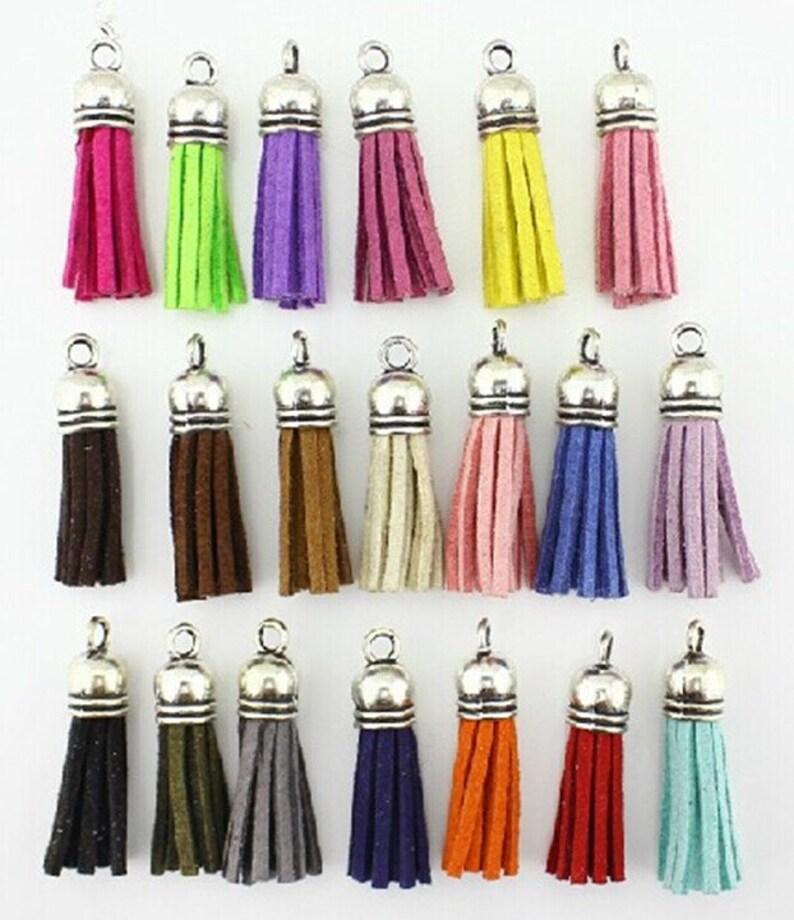 Puede incluir: Una colecci&oacute;n de colgantes de borlas coloridas con tapas y lazos de metal plateado. Las borlas vienen en varios colores, incluyendo rosa, verde, morado, burdeos, amarillo, marr&oacute;n, beige, rosa, azul y lavanda. Colores adicionales incluyen negro, verde oliva, gris, azul marino, naranja, rojo y turquesa.