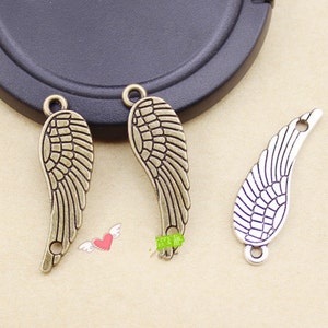 Könnte beinhalten: Drei Metall-Flügelanhänger in Bronze- und Silbertönen. Die Anhänger weisen detaillierte Federdesigns und kleine Schlaufen zum Befestigen an Schmuck oder anderen Bastelarbeiten auf. Die Flügel sind leicht gebogen und haben eine Vintage-Ästhetik.