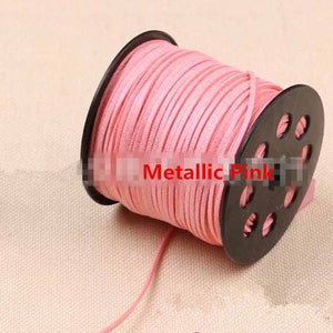 May include: A spool of metallic pink suede cord, wound around a black plastic spool with holes. The cord is approximately 2mm thick.