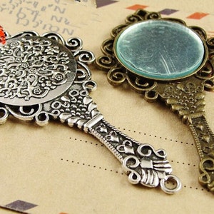 K&ouml;nnte beinhalten: Zwei verzierte Handspiegel aus Silber und Bronze mit aufwendigen Designs. Die Spiegel haben eine runde Form und sind mit Schn&ouml;rkeln und floralen Mustern verziert.