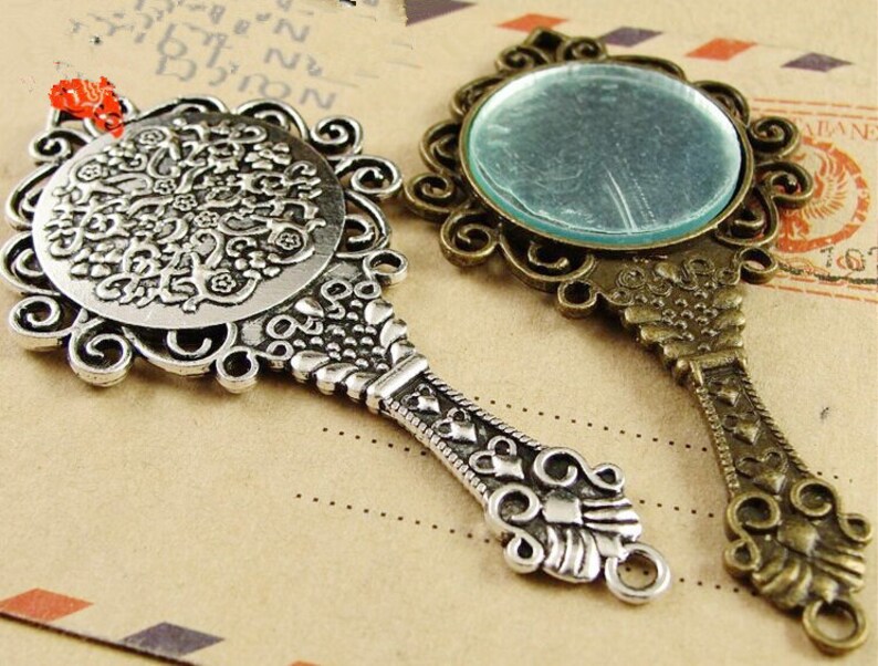 K&ouml;nnte beinhalten: Zwei verzierte Handspiegel aus Silber und Bronze mit aufwendigen Designs. Die Spiegel haben eine runde Form und sind mit Schn&ouml;rkeln und floralen Mustern verziert.