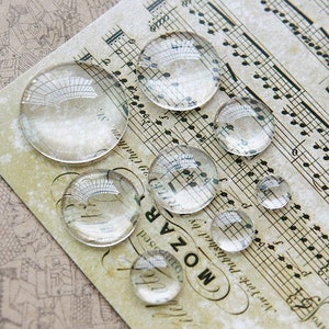 Peut inclure: Une collection de loupes en verre transparent de différentes tailles, disposées sur une feuille de musique avec le texte "MOZART" imprimé dessus.