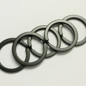May include: Five black metal key rings linked together. The rings are all different sizes and are arranged in a circle.