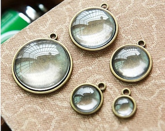 May include: Five round glass pendant charms with antique bronze metal frames. The charms are different sizes and are arranged on a brown surface.