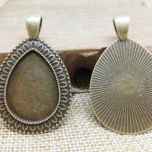 Könnte beinhalten: Zwei bronzefarbene Anhänger-Tabletts in Tropfenform. Ein Tablett hat einen dekorativen Rand und das andere ein Sonnenstrahlen-Design.