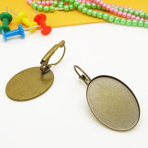 May include: Two oval-shaped earring settings with a bronze finish. The settings are designed to hold a cabochon stone or other embellishment. The earring backs are made of metal and have a spring-loaded closure.