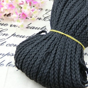 May include: A close-up of a black braided cord, wound into a coil. The cord is made of a soft, flexible material and has a smooth, even texture.
