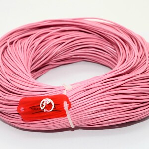 May include: A spool of pink leather cord, approximately 91 metres long, is wrapped around itself. The cord is smooth and has a slight sheen. The spool is labelled with a red tag that says "EMMA'S".