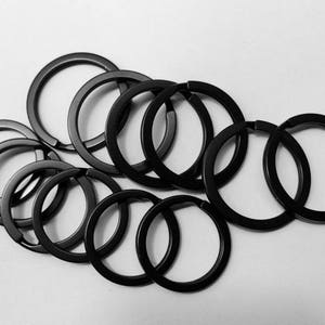 May include: A set of black metal key rings. The rings are all different sizes and are arranged in a circle.