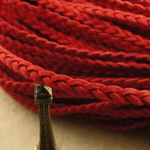 Puede incluir: Cordón de cuero trenzado rojo, un cordón grueso y tejido apretado con una textura suave y similar al ante.