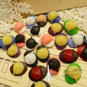Pode incluir: Conjunto de pingentes de coruja ovais coloridos com vários desenhos e cores, incluindo preto, branco, vermelho, verde, azul, rosa e amarelo.
