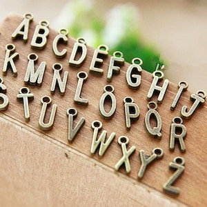 Könnte beinhalten: Ein Satz mit 26 antiken goldfarbenen Metall-Buchstabenanhängern. Jeder Buchstabe ist einzeln und hat eine kleine Schlaufe zum Anbringen an einer Halskette, einem Armband oder anderem Schmuck.