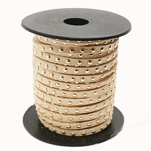 May include: A spool of beige leather cord with gold-colored studs. The cord is wrapped around a black spool.