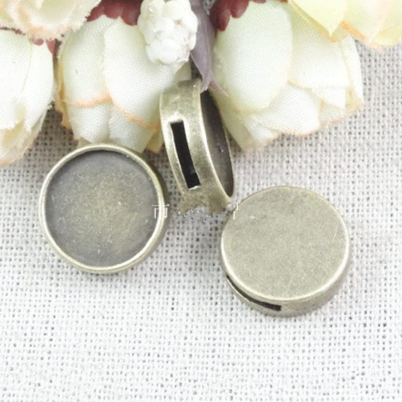 May include: Four antique gold-toned metal round pendant trays with a smooth, slightly textured surface. The trays are perfect for adding a personal touch to jewelry making projects.