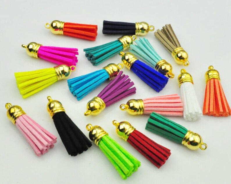 Puede incluir: Una colecci&oacute;n de borlas coloridas con tapas doradas. Las borlas est&aacute;n disponibles en varios tonos, incluyendo rosa, negro, verde, azul y naranja. Estas borlas decorativas son adecuadas para la fabricaci&oacute;n de joyas, manualidades o para a&ntilde;adir estilo a los accesorios.