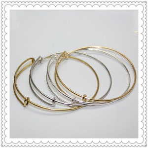 May include: Three expandable bangle bracelets in gold and silver tones. The bracelets are stacked on top of each other.