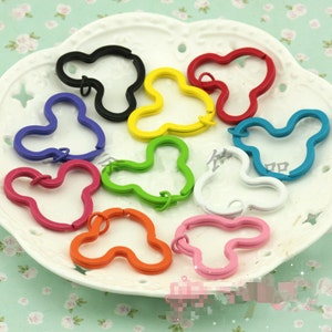 May include: Assortment of colorful metal keychains shaped like a Mickey Mouse head. The keychains are in various colors, including red, blue, green, yellow, orange, pink, and black.