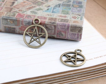 May include: Two antique gold-toned metal charms in the shape of a five-pointed star. The charms are on a white lined surface.