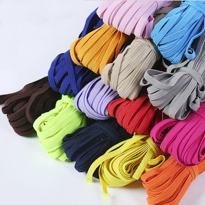 Könnte beinhalten: Eine Sammlung bunter Gummibänder in verschiedenen Farbtönen von Blau, Grün, Gelb, Orange, Rot, Rosa, Lila, Braun und Schwarz. Die Gummibänder sind in einem Stapel angeordnet, wobei sich einige Bänder überlappen.