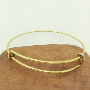 May include: A gold-toned expandable bangle bracelet with a simple design. The bracelet is made of metal and has a spring-loaded clasp.