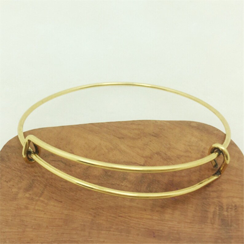 May include: A gold-toned expandable bangle bracelet with a simple design. The bracelet is made of metal and has a spring-loaded clasp.