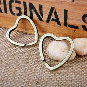 May include: Two antique gold heart-shaped key rings. The key rings are on a brown burlap surface.