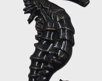 Puede incluir: Una figura de caballito de mar en tono bronce oscuro con un cuerpo segmentado, una aleta dorsal prominente a lo largo de la espalda y una cola enroscada. La superficie muestra un acabado metálico con crestas y texturas visibles.