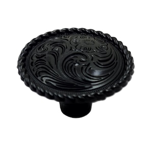 May include: A round black cabinet knob featuring an intricate embossed floral and swirling pattern on the face. The edge of the knob is finished with a decorative rope-style border, and it includes a cylindrical base for mounting purposes.