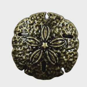 Könnte beinhalten: Ein kreisförmiges Sanddollar-Ornament mit metallischem Bronzefinish und einer dunklen, antik wirkenden Patina. Die Oberfläche hat eine texturierte, narbige Optik und zeigt in der Mitte ein markantes fünfblättriges Sternmuster mit kleinen Aussparungen.