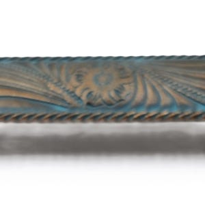 Puede incluir: Un tirador de armario rectangular con un acabado envejecido. El tirador presenta un patr&oacute;n detallado y ondulado en tonos azules y bronce, con un borde en forma de cuerda. Dos pomos de color marr&oacute;n oscuro proporcionan los puntos de montaje.