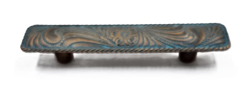Puede incluir: Un tirador de armario rectangular con un acabado envejecido. El tirador presenta un patr&oacute;n detallado y ondulado en tonos azules y bronce, con un borde en forma de cuerda. Dos pomos de color marr&oacute;n oscuro proporcionan los puntos de montaje.