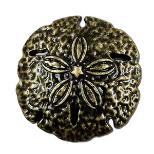 May include: A bronze-colored sand dollar with a textured surface and a detailed star-shaped design in the center. The sand dollar has a weathered appearance, with a dark bronze hue and a lighter gold-colored center.