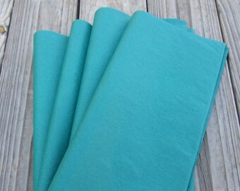 May include: Stack of teal tissue paper. The tissue paper is folded in half and the edges are visible.