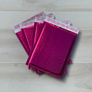 May include: A stack of five pink bubble mailers with a textured, metallic finish. The mailers have a self-adhesive seal.