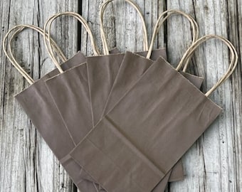 May include: Six brown paper gift bags with twisted paper handles. The bags are arranged in a fan shape on a wooden surface.
