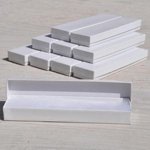 May include: A stack of white cardboard boxes, some open and some closed, with a single white box open on the bottom. The boxes are all the same size and shape, and they are made of a sturdy cardboard.