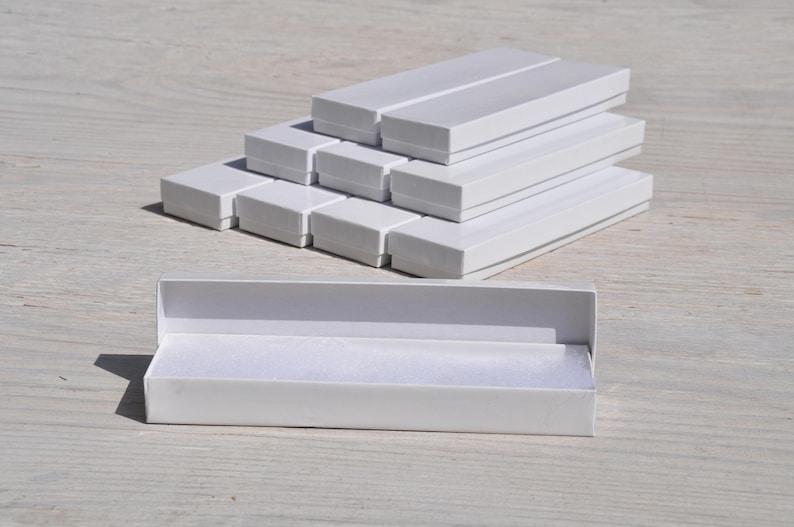 May include: A stack of white cardboard boxes, some open and some closed, with a single white box open on the bottom. The boxes are all the same size and shape, and they are made of a sturdy cardboard.