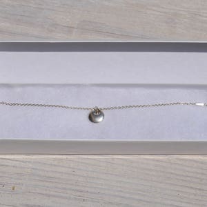 May include: A silver chain bracelet with a small, round pendant. The bracelet is in a white box with a white background.