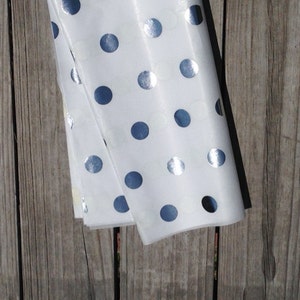 Pu&ograve; includere: Carta velina bianca con pois argentati. La carta &egrave; piegata a met&agrave; e si trova su una superficie di legno.