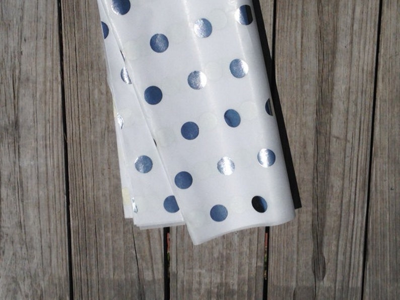 Pu&ograve; includere: Carta velina bianca con pois argentati. La carta &egrave; piegata a met&agrave; e si trova su una superficie di legno.