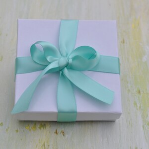 May include: A white gift box with a light blue satin ribbon tied in a bow.