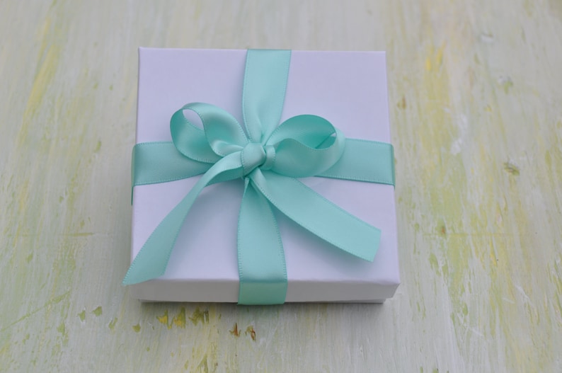 May include: A white gift box with a light blue satin ribbon tied in a bow.