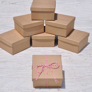May include: A stack of six brown cardboard boxes, with the top box tied with a red and white twine bow. The boxes are arranged in a pyramid shape on a white wooden surface.