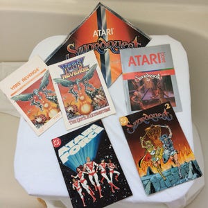 May include: A collection of vintage Atari video game cartridges and comic books. The cartridges include Yars' Revenge, Yar's Revenge, Swordquest, and Swordquest 2. The comic books include Atari Force and Swordquest.