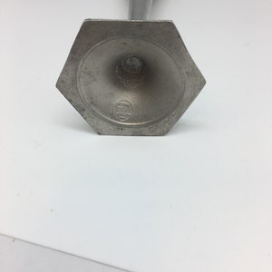 Pu&ograve; includere: Un candeliere color peltro con base esagonale e stelo sottile e decorato. La base presenta un'indentazione circolare con un piccolo stemma. Il candeliere &egrave; in metallo e ha un aspetto vintage.